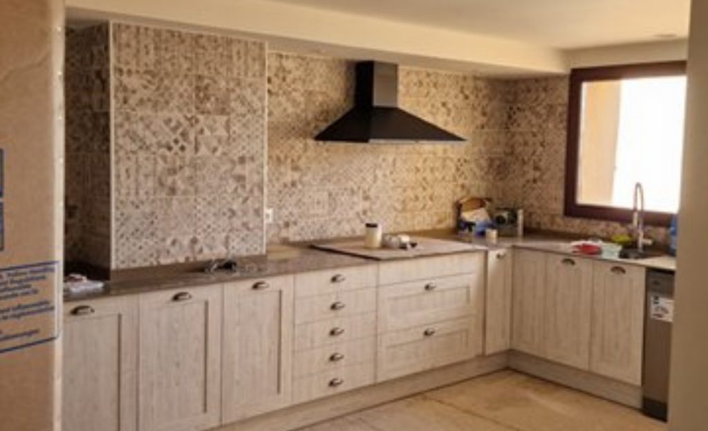 Cocina equipada de estilo rústico con muebles de madera clara, encimera, fregadero y campana extractora